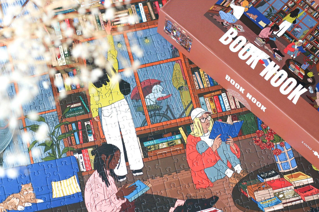 Book Nook jigsaw puzzle box next to a close up of the completed puzzle featuring people reading inside a library.
