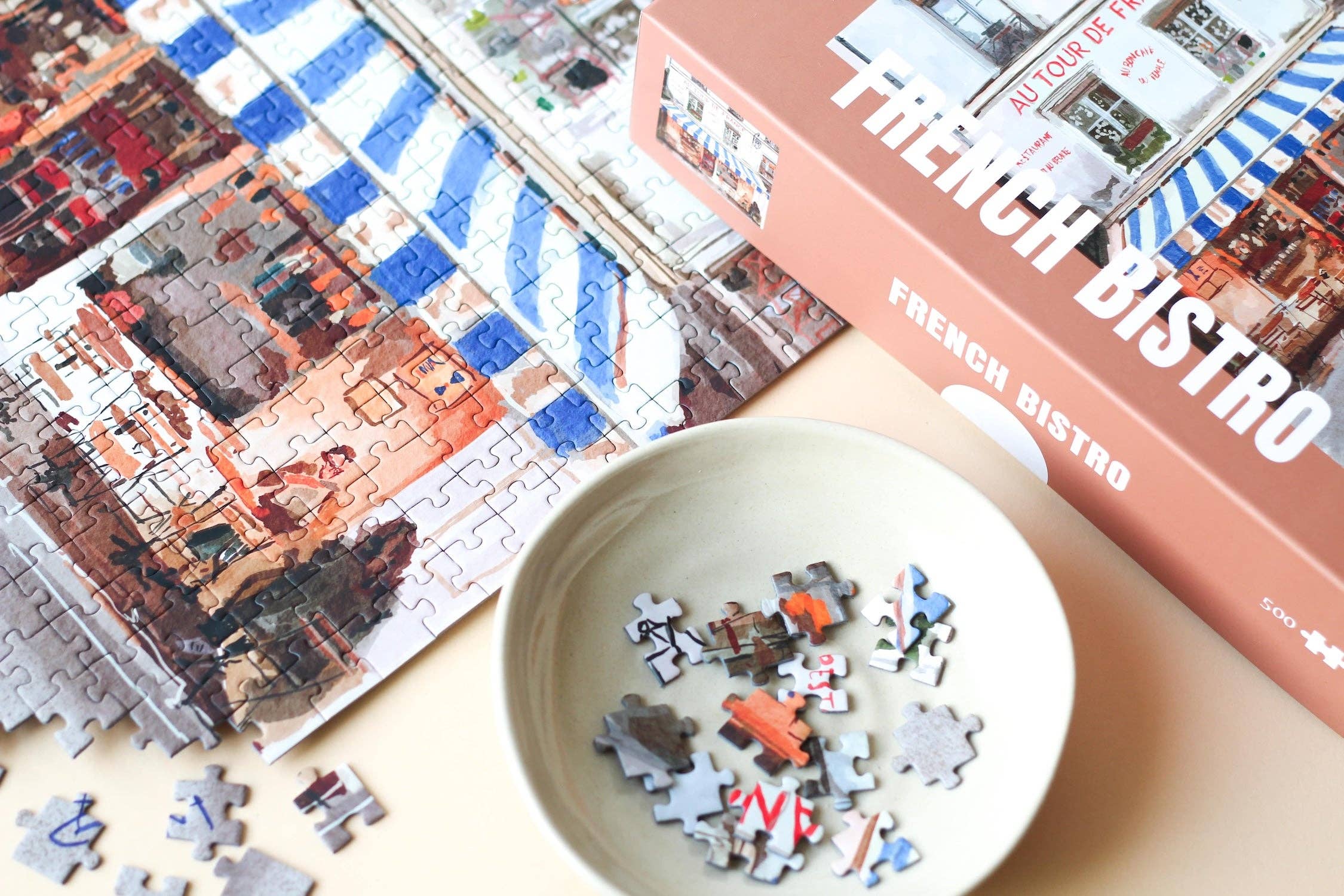 French Bistro jigsaw puzzle partially completed next to a puzzle box.