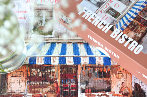 Jigsaw puzzle with a completed section showing a French bistro scene, with a box labeled 'French Bistro' in the foreground.