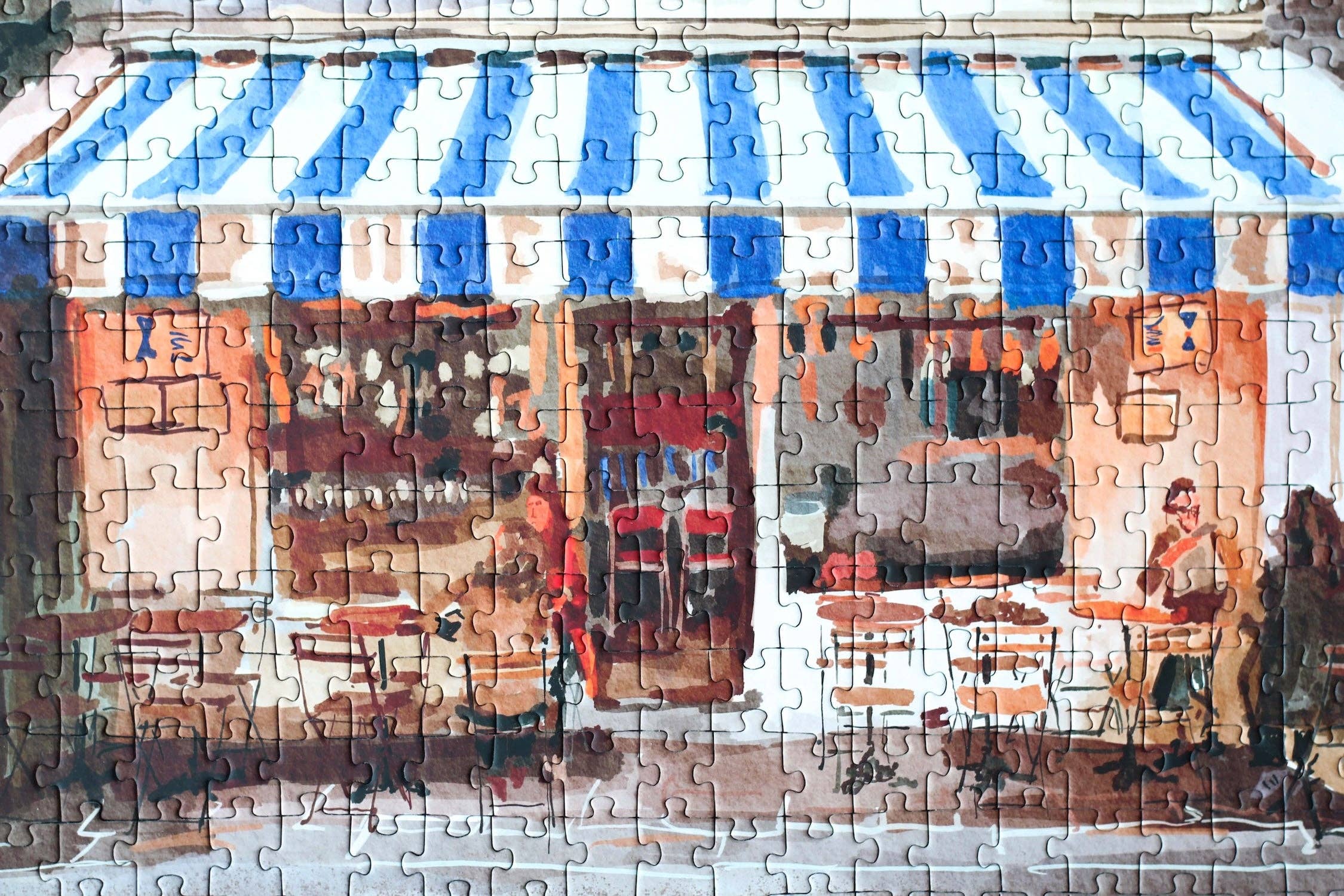 Partial puzzle of a street scene with people and tables under blue and white striped awnings.
